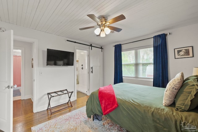 bedroom with a barn door, ceiling fan, hardwood / wood-style floors, and ensuite bath