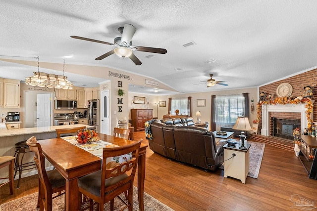 dining room with ceiling fan, wood-type flooring, a textured ceiling, lofted ceiling, and a fireplace