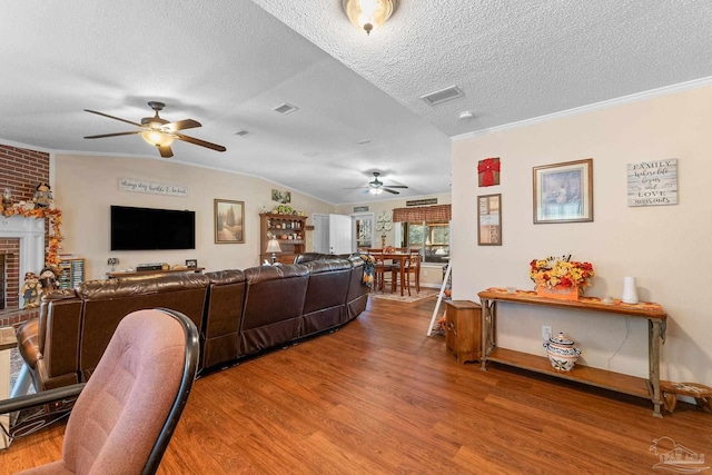 living room featuring hardwood / wood-style floors, lofted ceiling, crown molding, a fireplace, and a textured ceiling