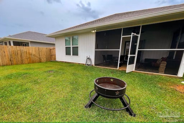 rear view of property featuring fence, a fire pit, a sunroom, and a yard