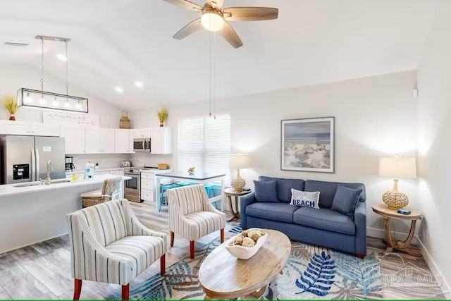 living area with vaulted ceiling, a ceiling fan, light wood-type flooring, baseboards, and visible vents