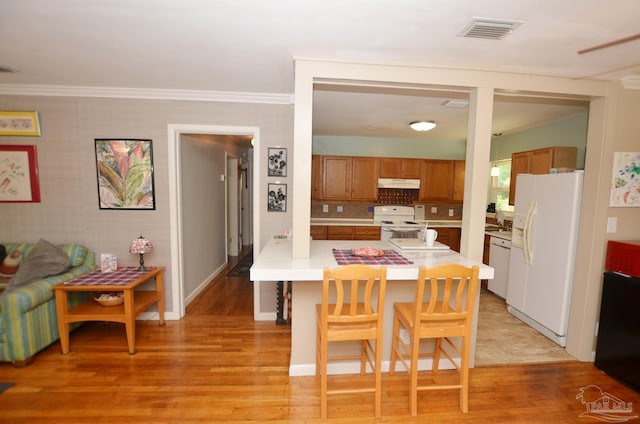 2153 Bergren Rd, Gulf Breeze, FL 32563 - kitchen featuring white appliances, under cabinet range hood, light countertops, brown cabinetry, and a breakfast bar