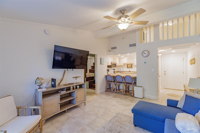 tiled living room with ceiling fan, a high ceiling, and ornamental molding