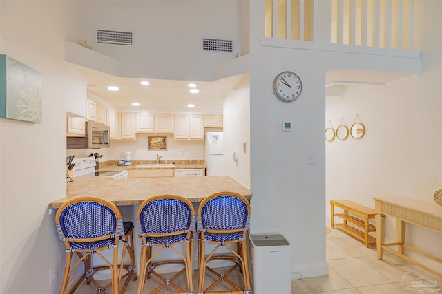 kitchen with light tile patterned floors, kitchen peninsula, a breakfast bar area, white appliances, and sink