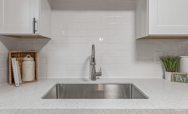 details with white cabinets, tasteful backsplash, light stone countertops, and a sink