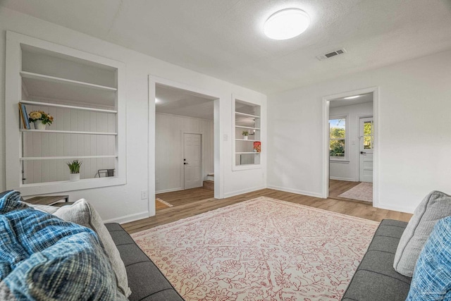living area featuring baseboards, built in features, wood finished floors, and visible vents
