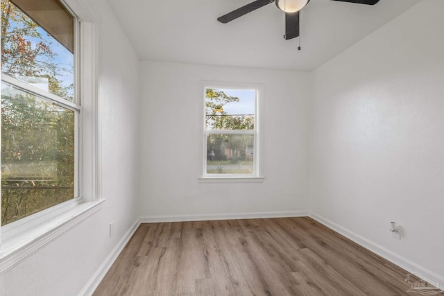 empty room with ceiling fan, a wealth of natural light, wood finished floors, and baseboards