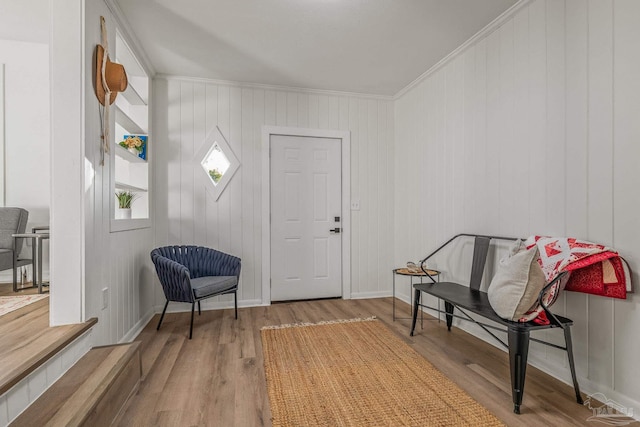 living area featuring wooden walls, wood finished floors, baseboards, and ornamental molding