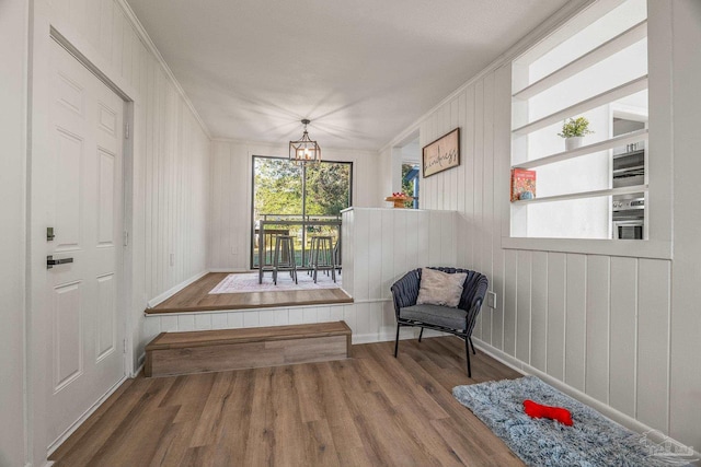 sitting room featuring wooden walls, wood finished floors, crown molding, baseboards, and a notable chandelier