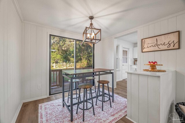 dining area featuring a chandelier, wood finished floors, baseboards, and ornamental molding