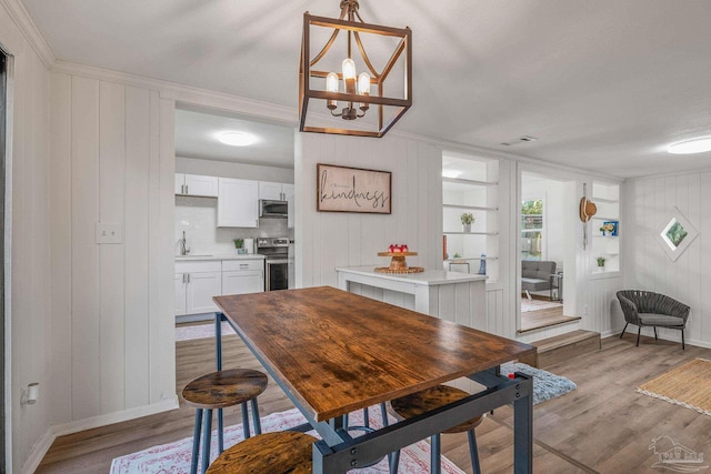 dining room with light wood finished floors, an inviting chandelier, visible vents, crown molding, and baseboards