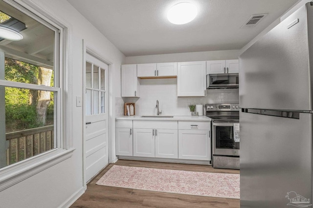 kitchen featuring white cabinets, a sink, visible vents, decorative backsplash, and appliances with stainless steel finishes