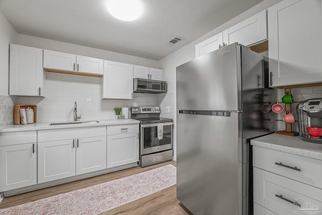 kitchen featuring light wood finished floors, light countertops, visible vents, a sink, and appliances with stainless steel finishes