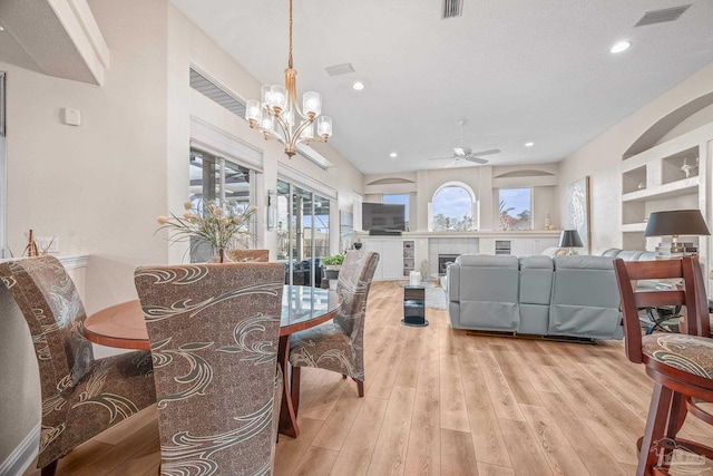 dining space with visible vents, a tiled fireplace, light wood-style flooring, ceiling fan with notable chandelier, and recessed lighting