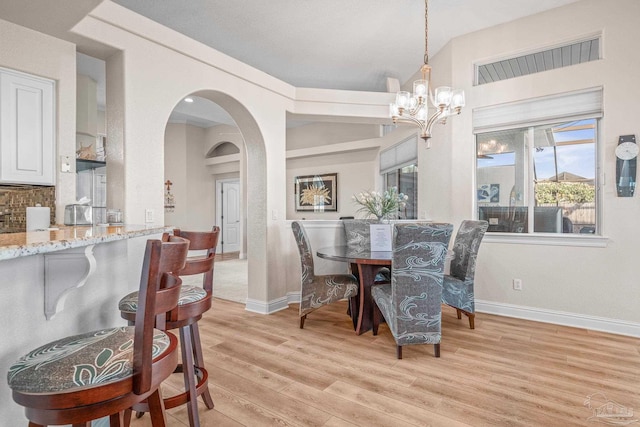 dining area featuring light wood-style floors, baseboards, arched walkways, and a chandelier