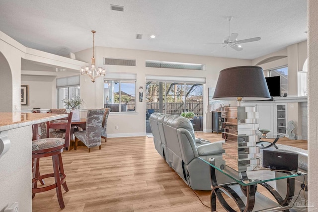 living room featuring visible vents, a textured ceiling, light wood finished floors, and ceiling fan with notable chandelier