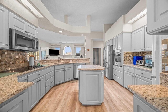 kitchen with light wood finished floors, appliances with stainless steel finishes, a sink, gray cabinets, and backsplash