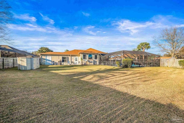 rear view of property featuring glass enclosure, fence, and a lawn