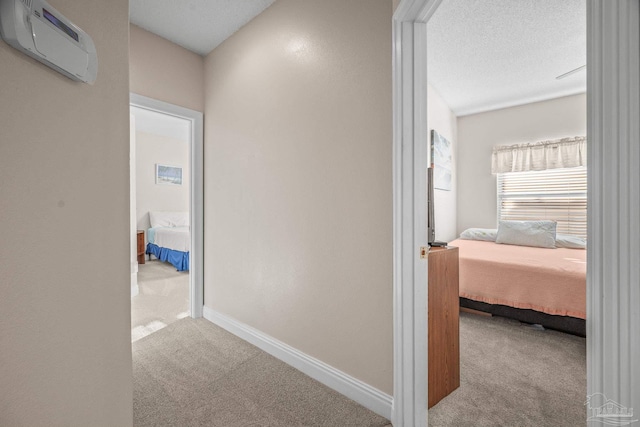 hallway with a textured ceiling, carpet floors, a wall mounted AC, and baseboards