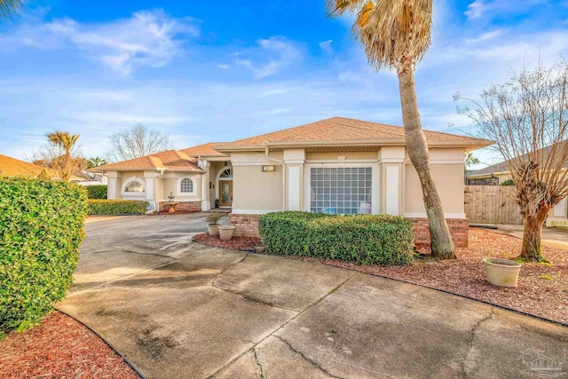 view of front of home featuring driveway, brick siding, fence, and stucco siding