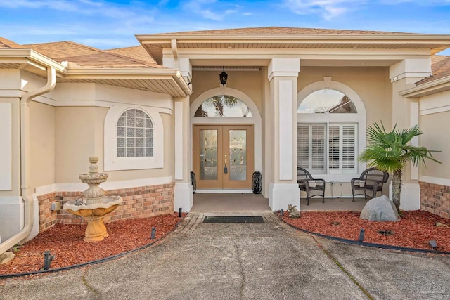 entrance to property with stucco siding, roof with shingles, brick siding, and french doors