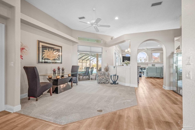 living area featuring ceiling fan with notable chandelier, hardwood / wood-style flooring, visible vents, and baseboards