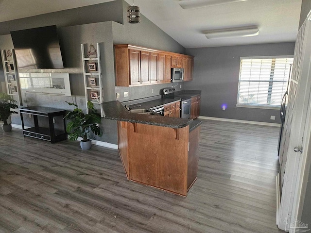 kitchen featuring brown cabinetry, dark wood finished floors, dark countertops, appliances with stainless steel finishes, and a sink