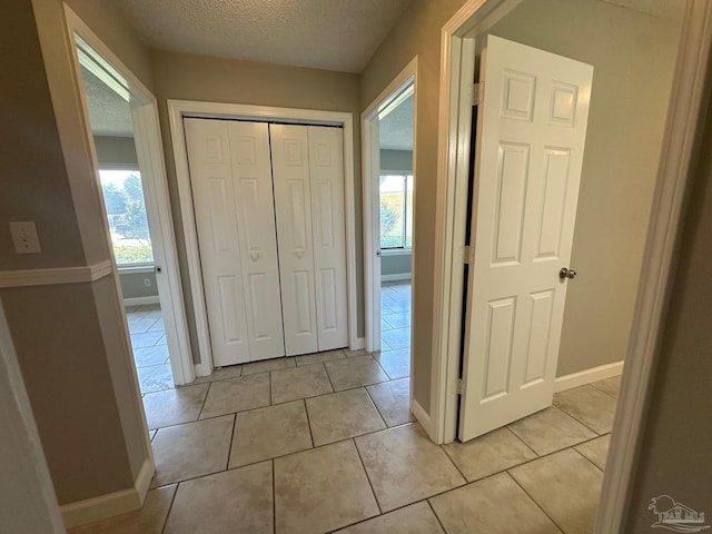 hallway featuring a healthy amount of sunlight, light tile patterned floors, and a textured ceiling