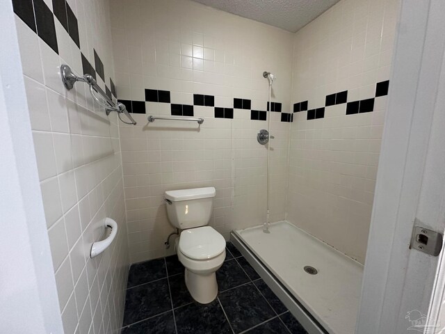 bathroom with tiled shower, tile patterned floors, toilet, tile walls, and a textured ceiling