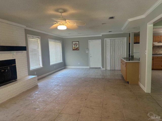 unfurnished living room featuring light tile patterned floors, ceiling fan, ornamental molding, a textured ceiling, and a brick fireplace