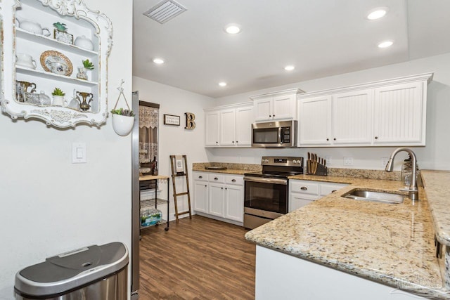 kitchen with kitchen peninsula, appliances with stainless steel finishes, light stone countertops, sink, and white cabinets