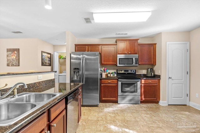 kitchen featuring appliances with stainless steel finishes, dark stone counters, a textured ceiling, sink, and washer / clothes dryer