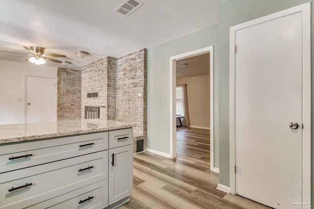 kitchen with light stone counters, baseboards, visible vents, light wood-style flooring, and ceiling fan