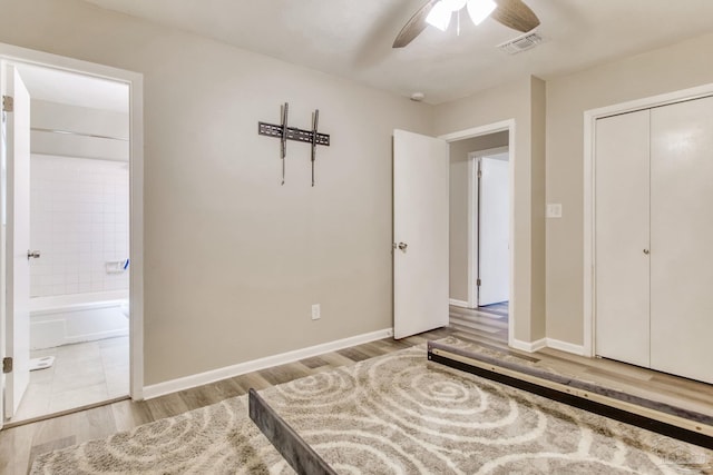 bedroom with baseboards, wood finished floors, visible vents, and connected bathroom