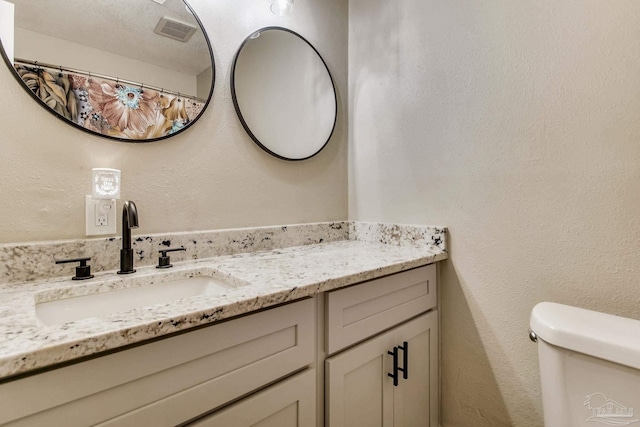 full bath with visible vents, toilet, a textured ceiling, vanity, and a textured wall