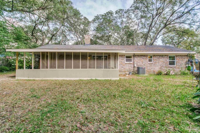 rear view of house with central AC unit, a yard, a sunroom, a chimney, and brick siding