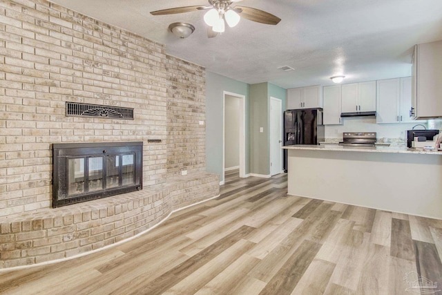 kitchen featuring a ceiling fan, under cabinet range hood, stainless steel electric range, a fireplace, and black refrigerator with ice dispenser