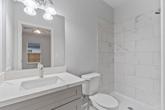 bathroom with a tile shower, vanity, toilet, and ceiling fan