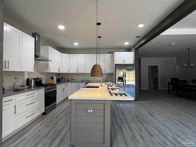 kitchen featuring wall chimney exhaust hood, decorative backsplash, a center island with sink, white cabinets, and appliances with stainless steel finishes