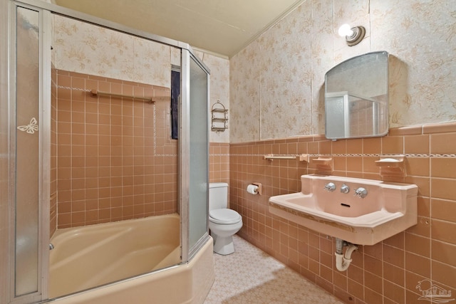 full bathroom with toilet, shower / bath combination with glass door, sink, and tile walls