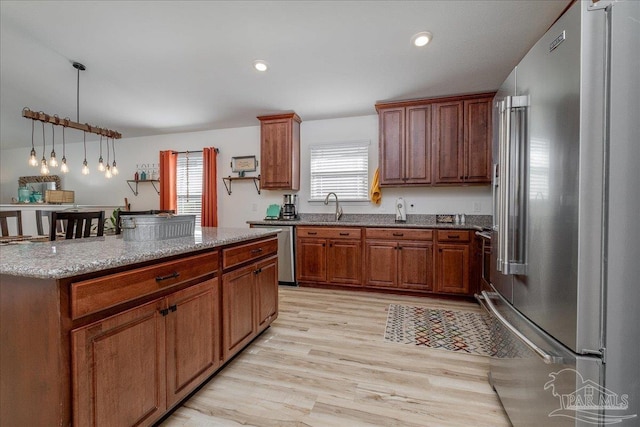 kitchen featuring sink, light stone counters, light hardwood / wood-style flooring, pendant lighting, and stainless steel appliances