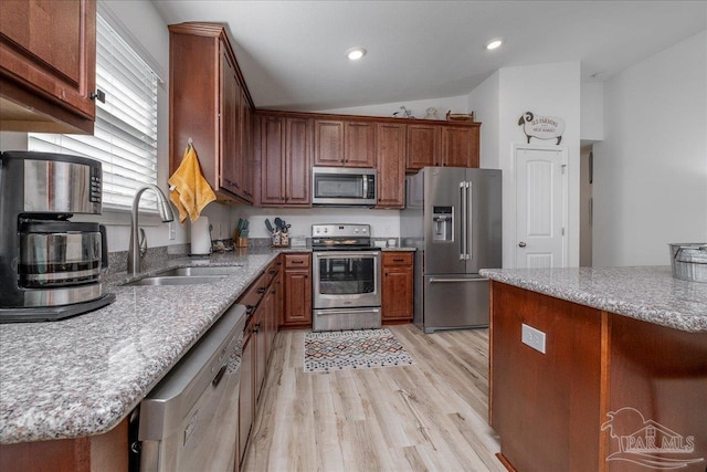 kitchen with lofted ceiling, sink, light stone counters, stainless steel appliances, and light wood-type flooring