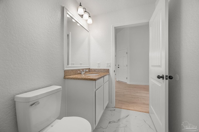 half bathroom with vanity, a textured wall, toilet, and marble finish floor