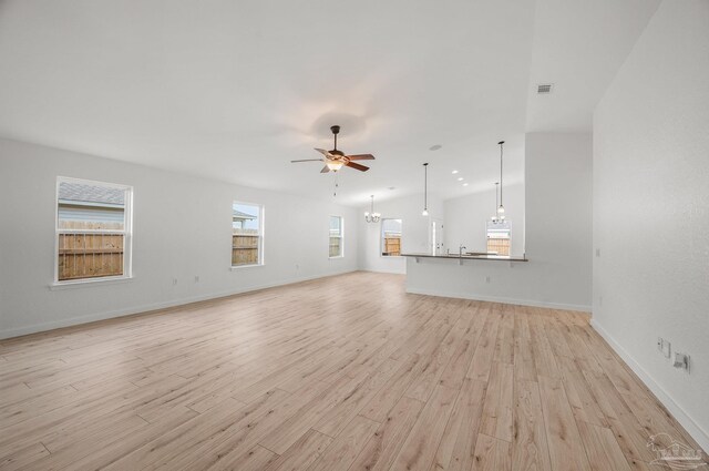 unfurnished living room with visible vents, plenty of natural light, light wood-style flooring, and ceiling fan with notable chandelier
