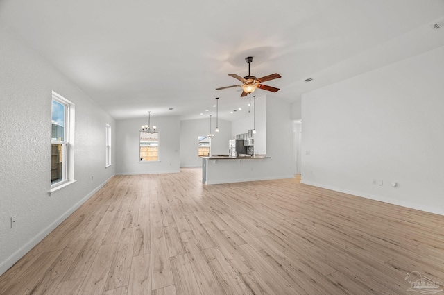 unfurnished living room featuring light wood-style floors, ceiling fan with notable chandelier, baseboards, lofted ceiling, and visible vents