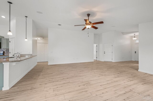 unfurnished living room featuring ceiling fan, visible vents, a sink, baseboards, and light wood-style flooring
