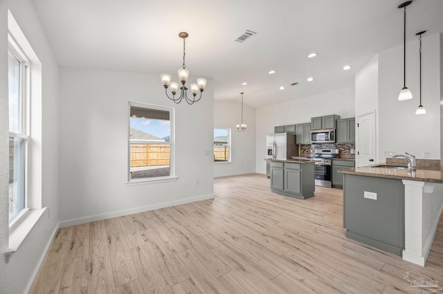 kitchen featuring appliances with stainless steel finishes, a center island, gray cabinetry, light wood finished floors, and a notable chandelier