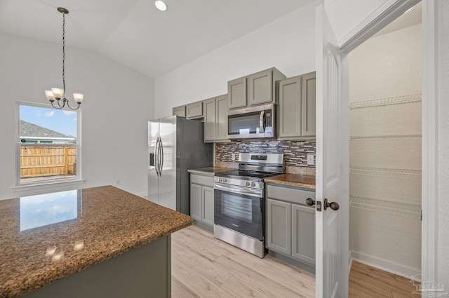 kitchen with appliances with stainless steel finishes, lofted ceiling, light wood-type flooring, backsplash, and gray cabinetry