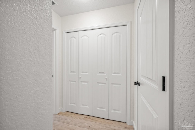 hall featuring a textured ceiling, a textured wall, visible vents, and light wood-type flooring
