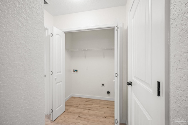 laundry room featuring a textured wall, laundry area, hookup for a washing machine, electric dryer hookup, and light wood-type flooring